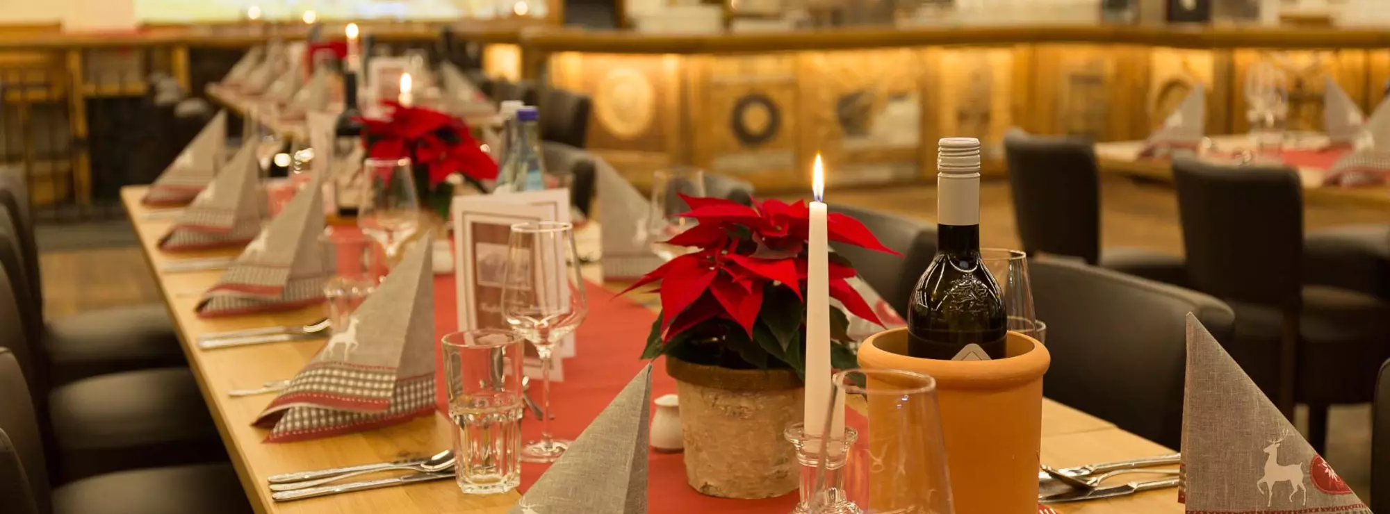 Rot gedeckter Tisch mit Weihnachtsstern und Kerzen und Weinflaschen