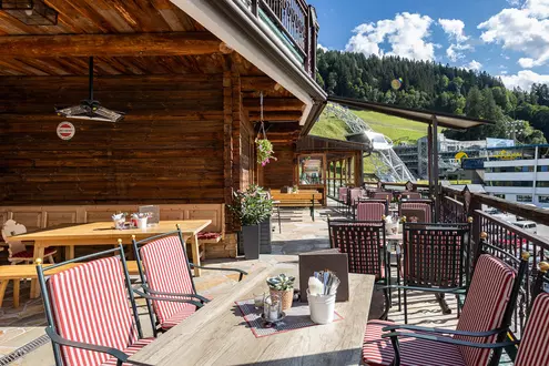 Restaurantterrasse mit Bergblick im Sommer mit Holztischen und Topfpflanzen